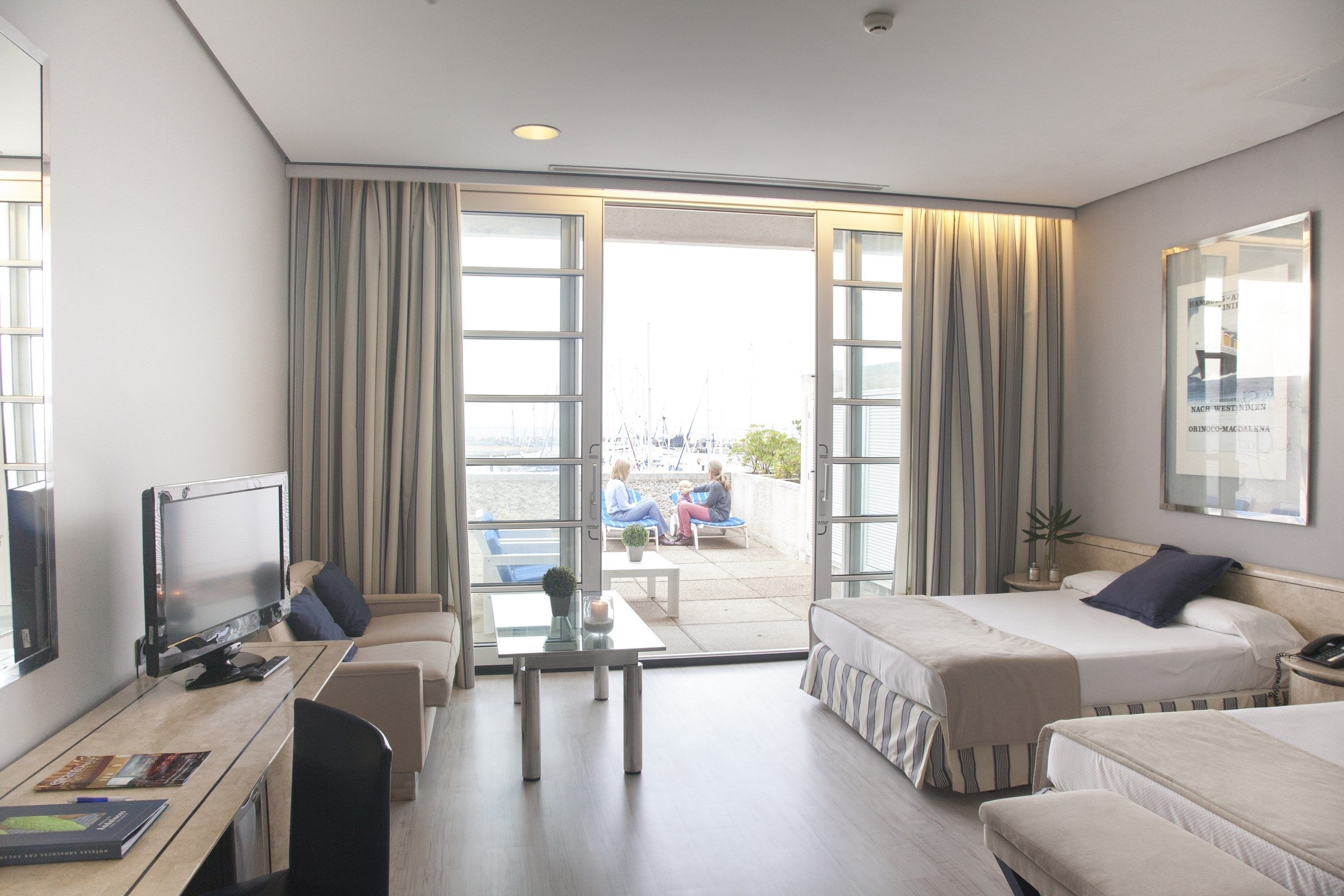 A hotel room with two beds, a desk, a TV, and a balcony with a view.