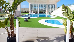 Un bâtiment moderne doté de grandes fenêtres, d’une piscine et d’une pelouse artificielle verdoyante.