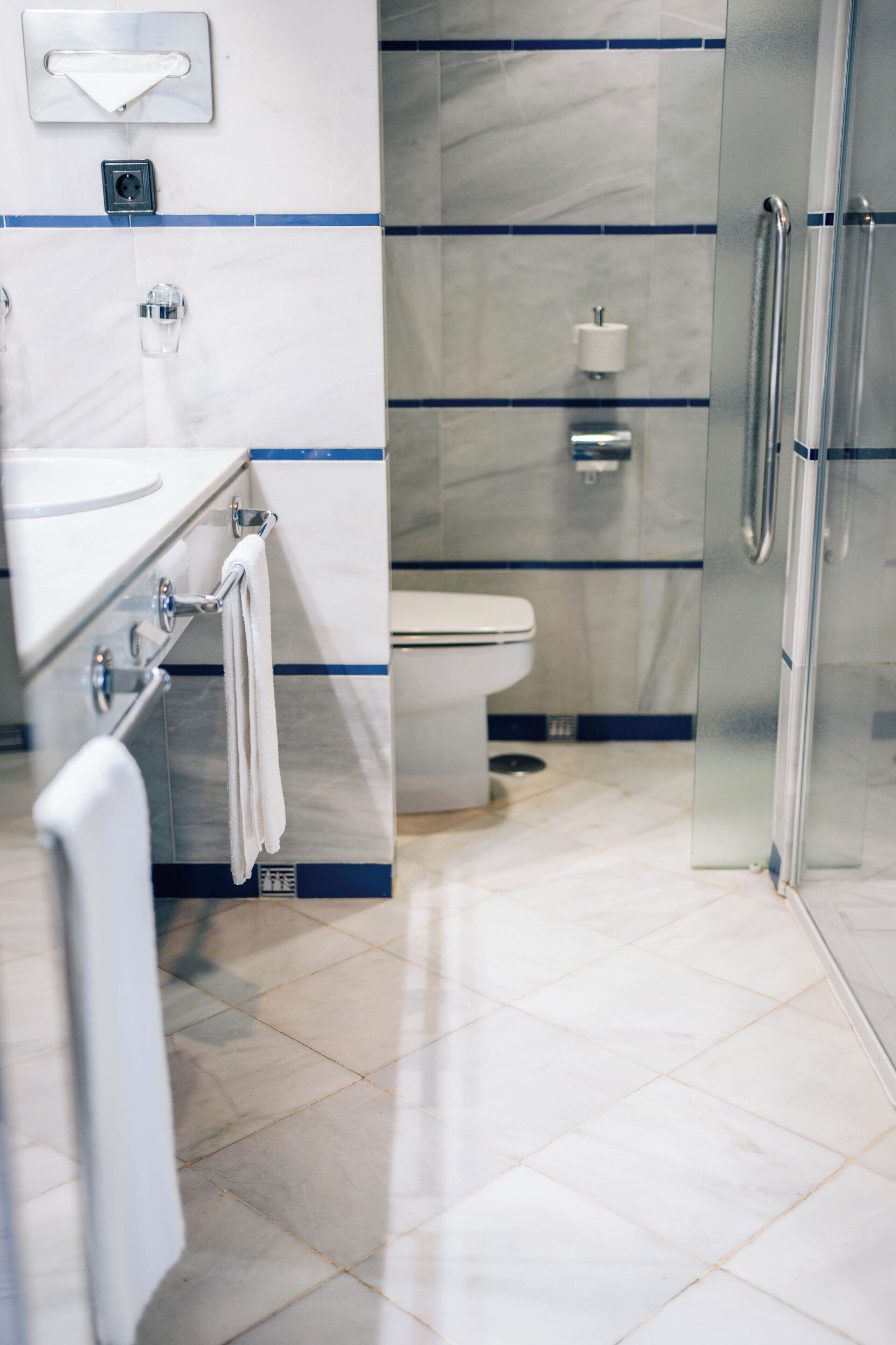 Un baño moderno con cabina de ducha de vidrio, inodoro blanco y lavamanos con toallero.