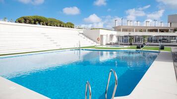 A swimming pool with clear blue water, a white poolside area, and a staircase leading to a building with a white facade.