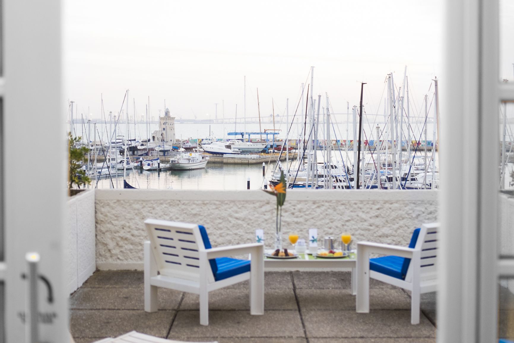 A balcony with two white chairs and a table, overlooking a marina with numerous boats.