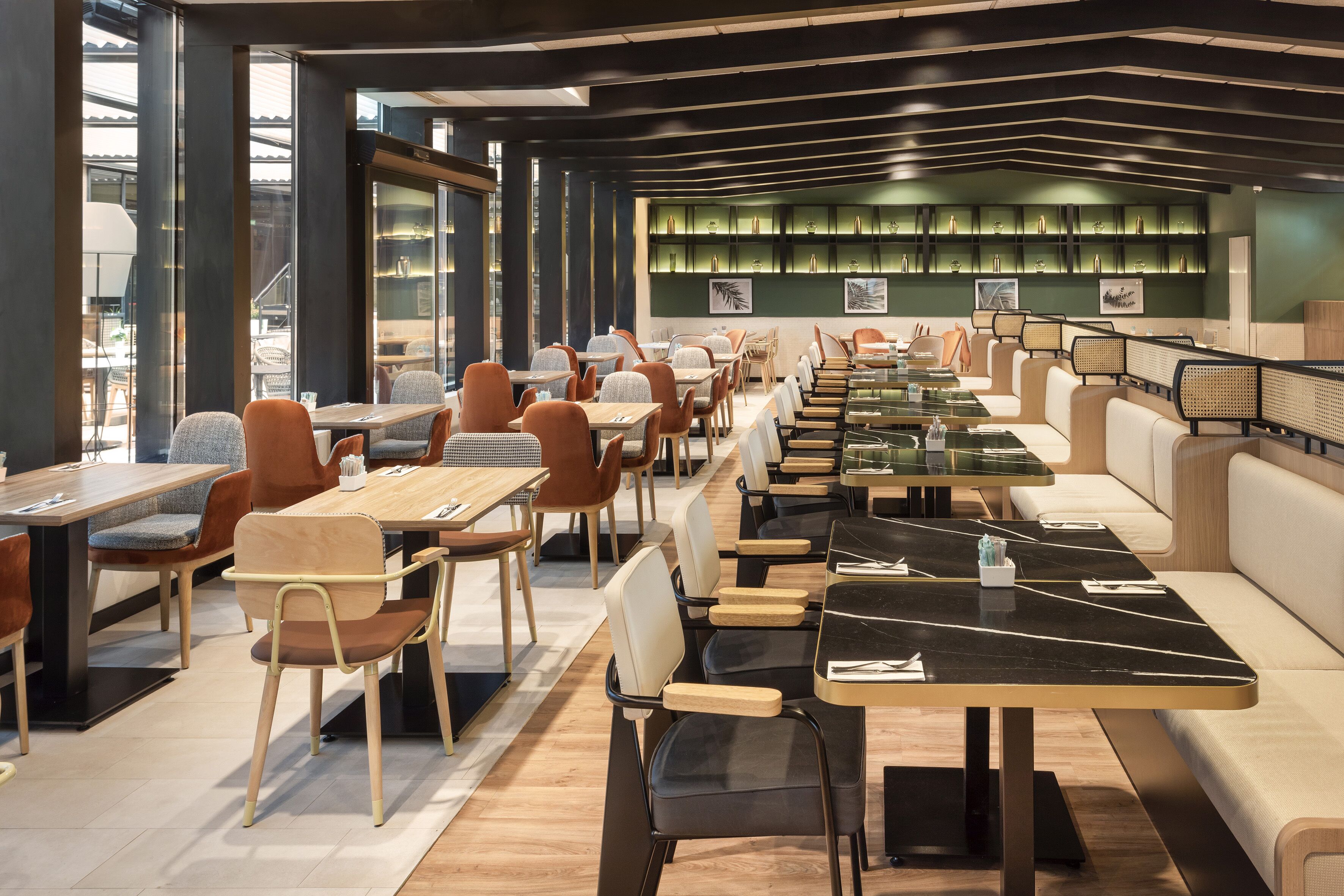 Un restaurante moderno con largas mesas compartidas y cabinas, que presenta una pared verde con elementos decorativos y vistas al exterior.