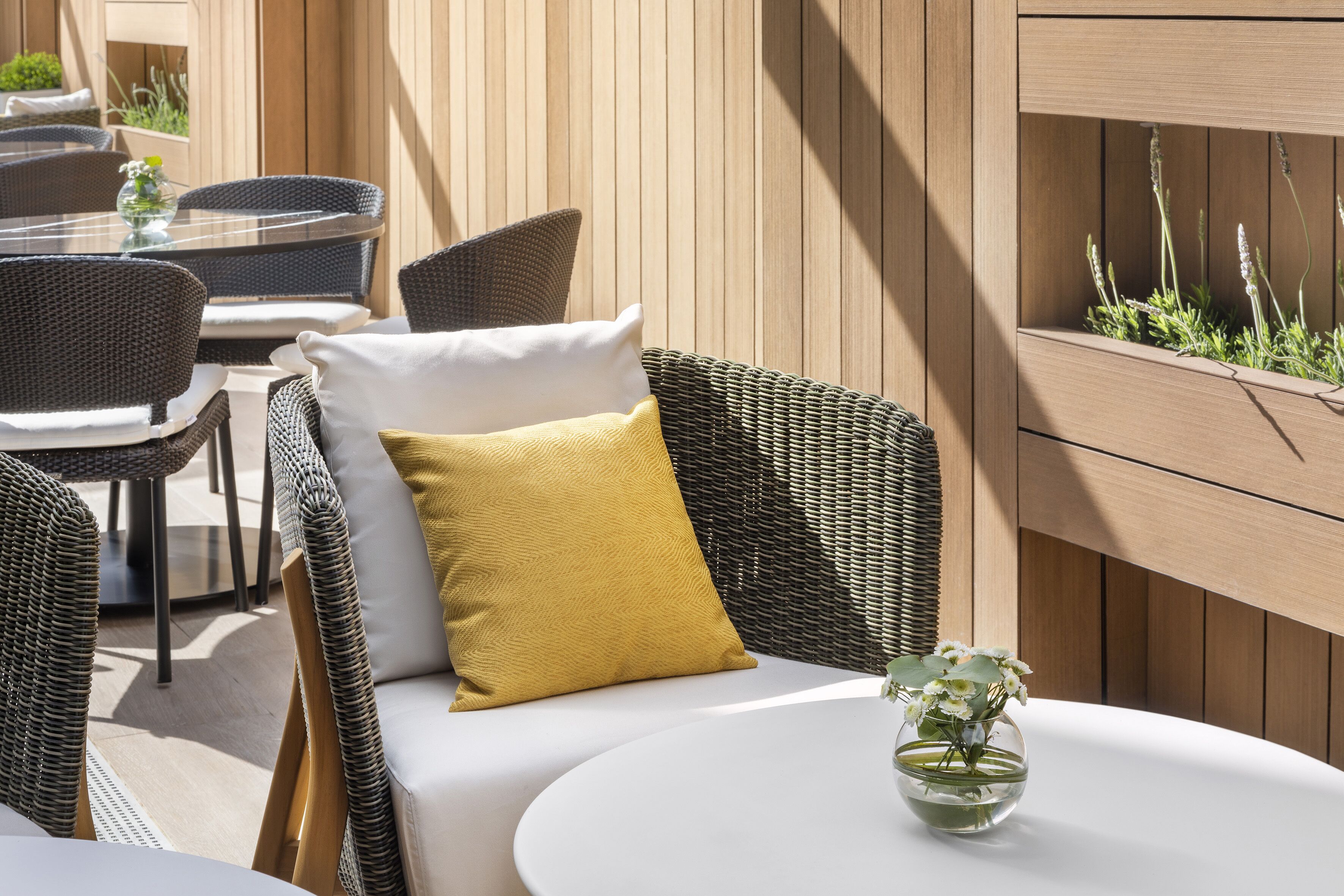 A wicker sofa with cushions, a round table, and a planter with plants.
