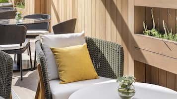 A wicker sofa with cushions, a round table, and a planter with plants.