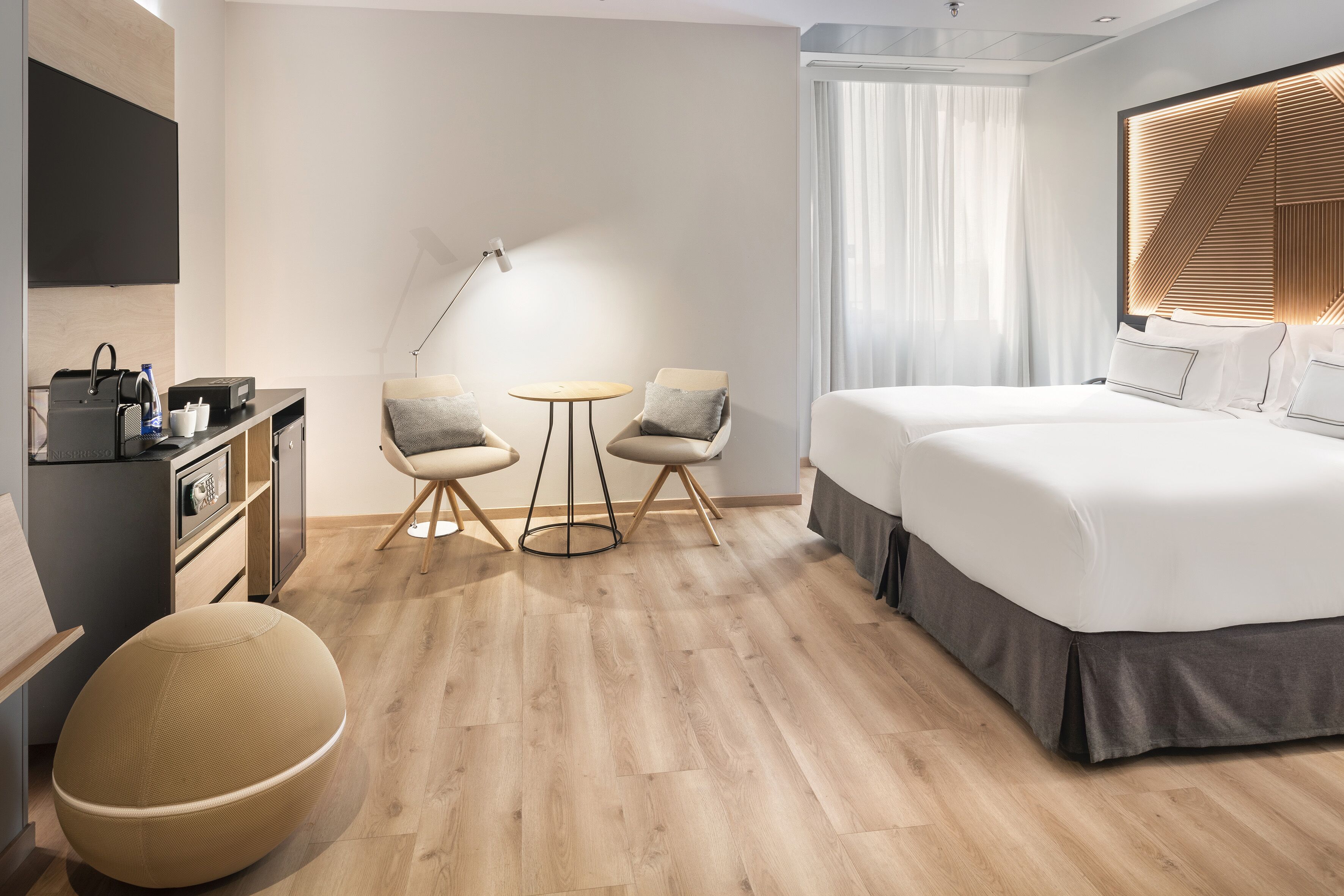 Een moderne hotelkamer met een groot bed, een bureau met een computer, een stoel, een ronde tafel en een groot raam met gordijnen.