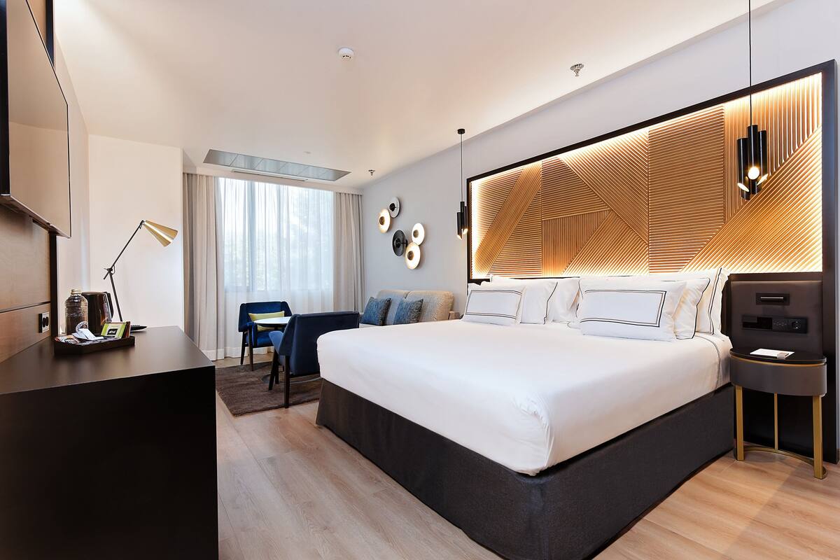 A modern hotel room with a large bed, a desk, and a TV.
