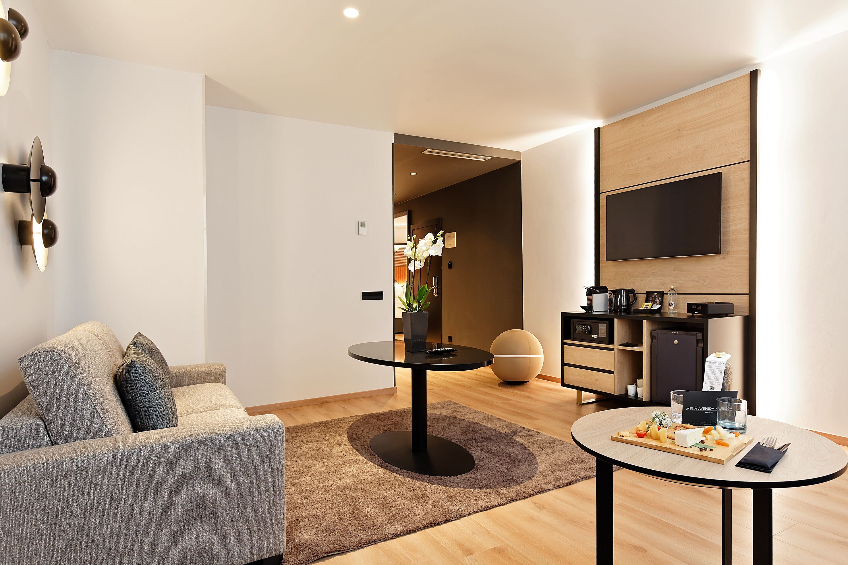A modern living room with a sofa, a round coffee table, and a flat-screen TV mounted on the wall.