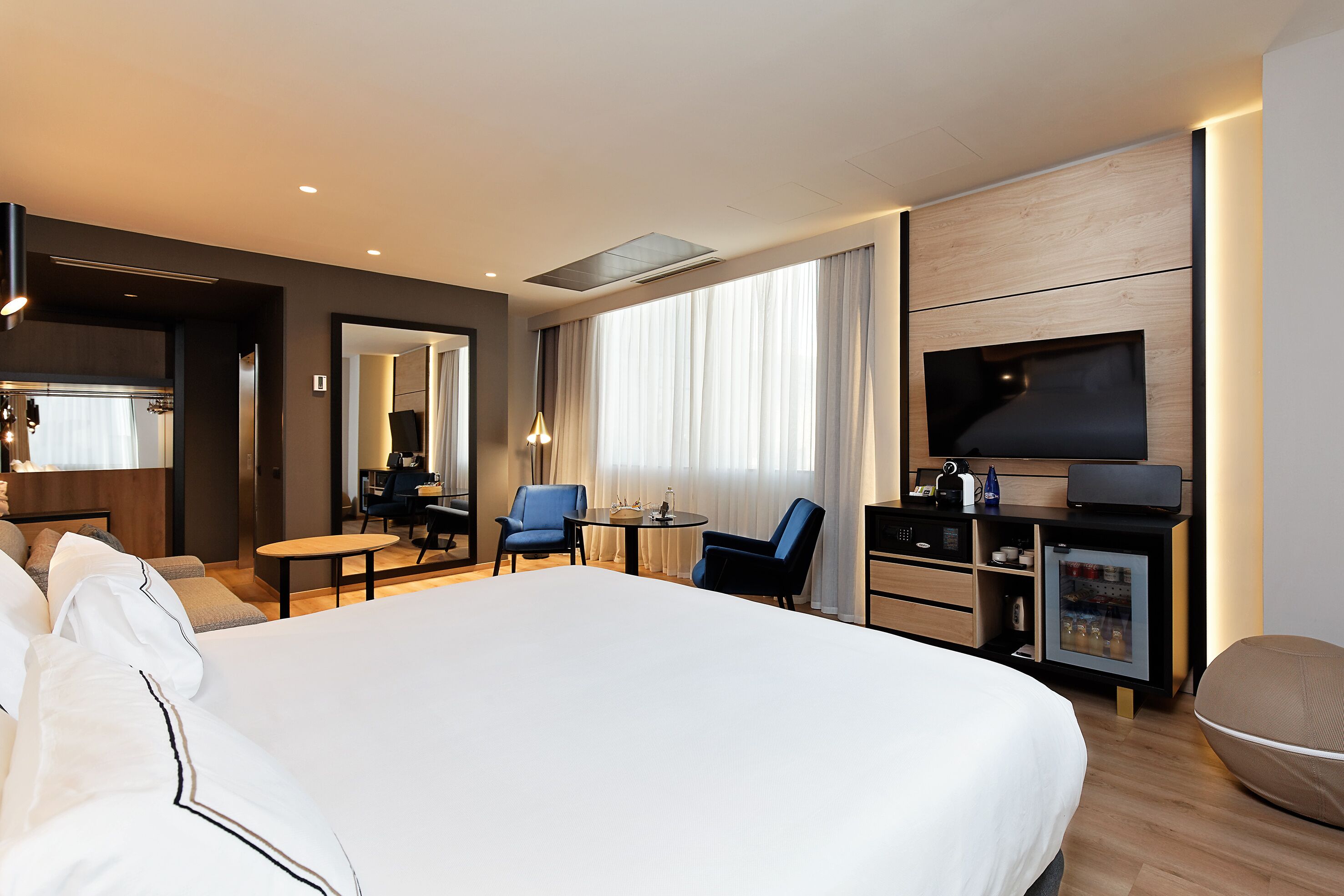 Een moderne hotelkamer met een groot bed, een bureau met stoel, een televisie en een minibar.