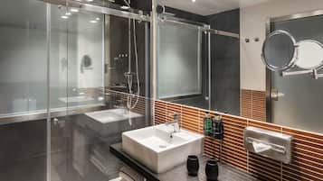Un baño moderno con cabina de ducha de vidrio, un lavamanos grande y un mueble de tocador con dispensador de toallas.