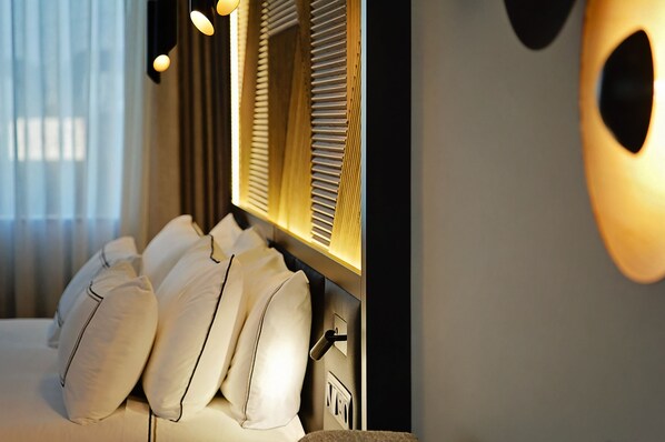 Una habitación de hotel con cama, almohadas, mesita de noche y espejo.