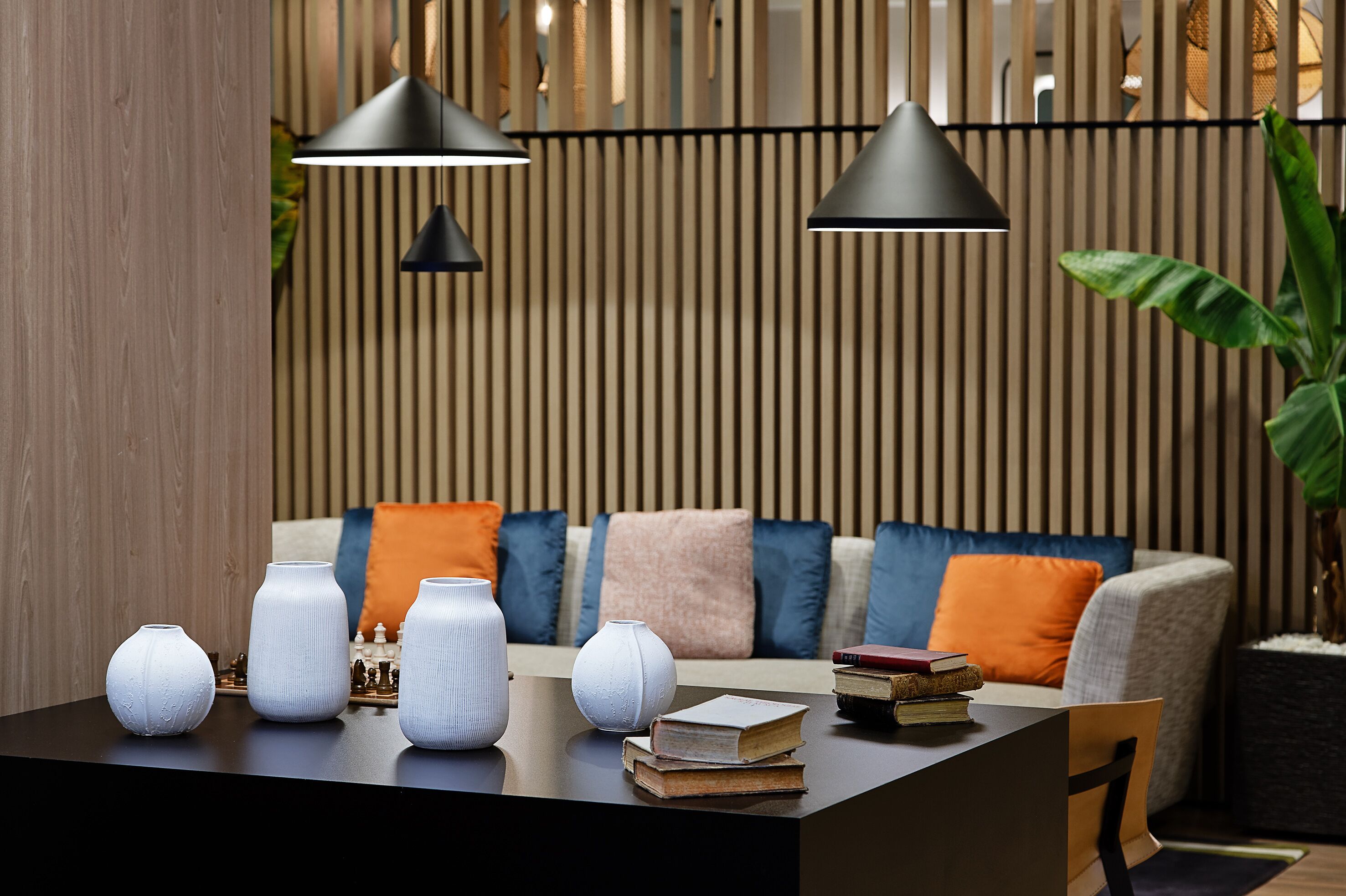 Una sala de estar moderna con sofá, cojines, una mesa de centro con jarrones y libros, e iluminación colgante.