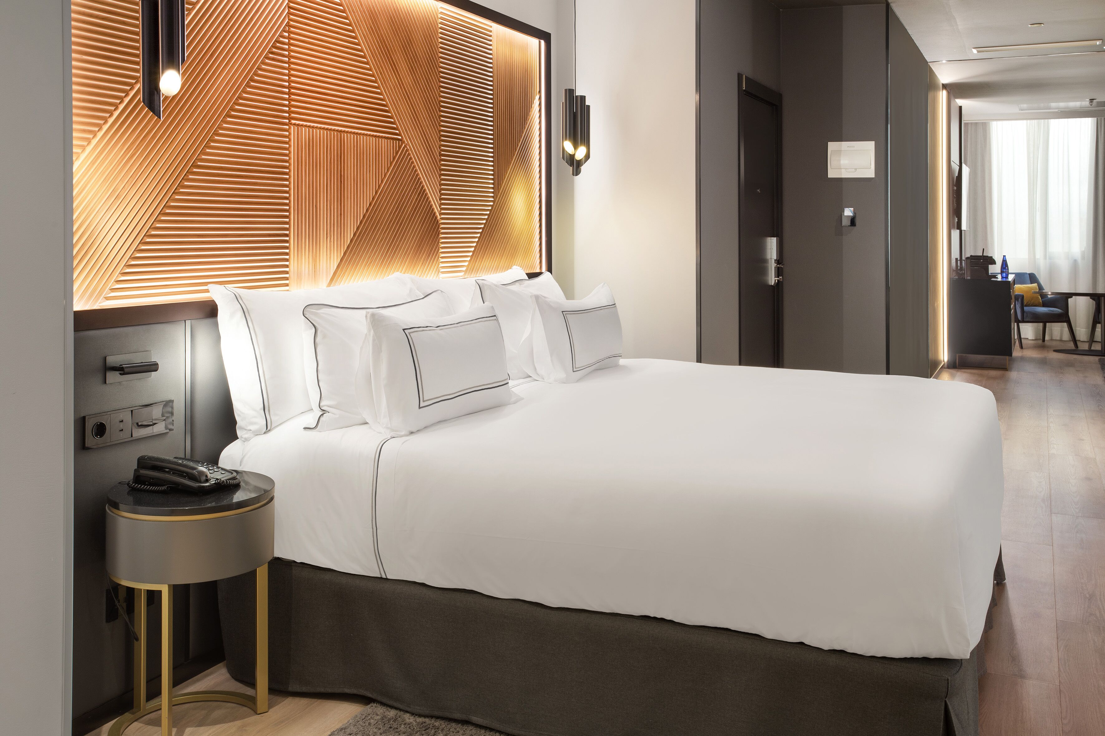 Una habitación de hotel moderna con una cama grande, una mesita de noche con teléfono y una pared con diseño geométrico.