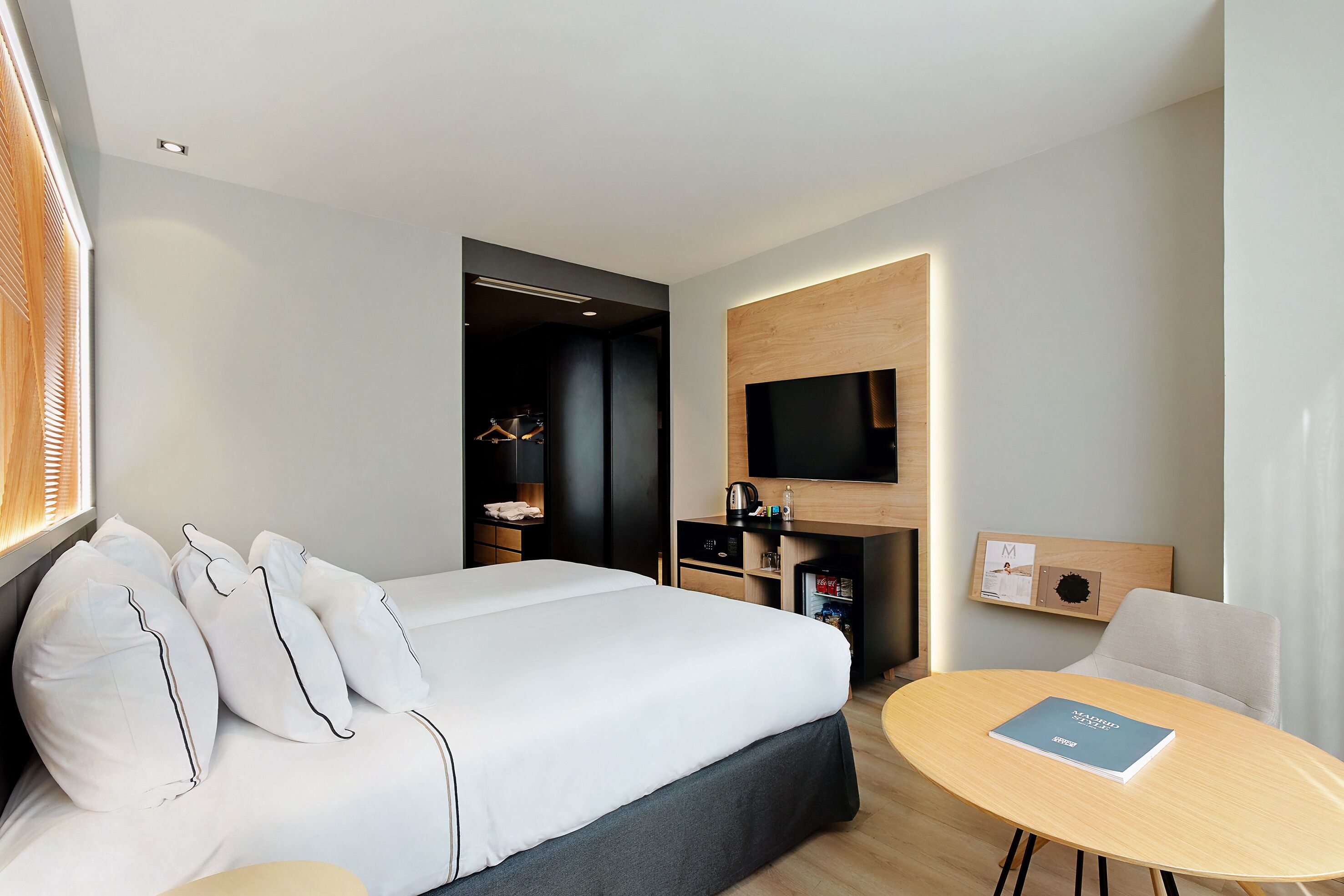 Una camera d'albergo moderna con un letto grande, un tavolino, una TV a parete e un armadietto in legno.