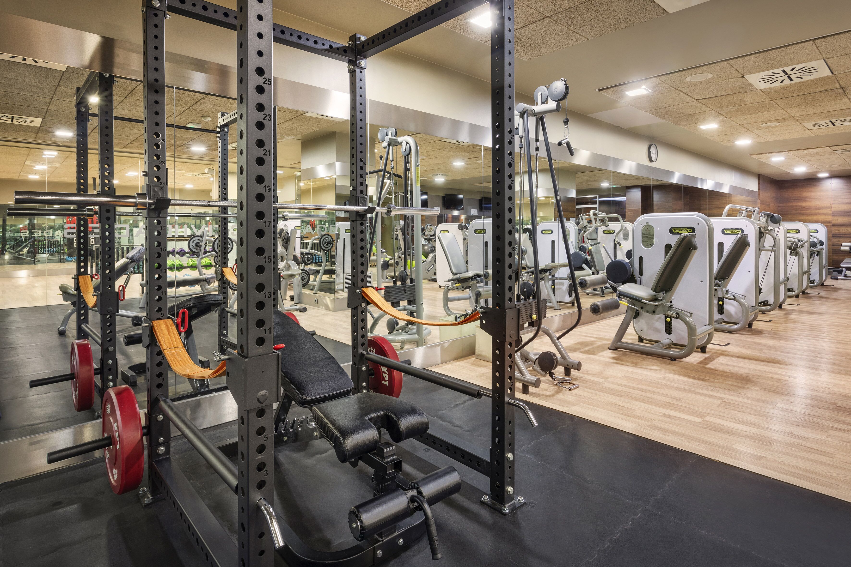 Une salle de sport équipée de matériel de musculation, de machines d’exercice et dotée d’un mur recouvert de miroirs.