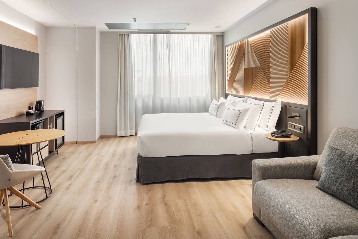 A modern hotel room with a large bed, a sofa, a desk, and a TV.