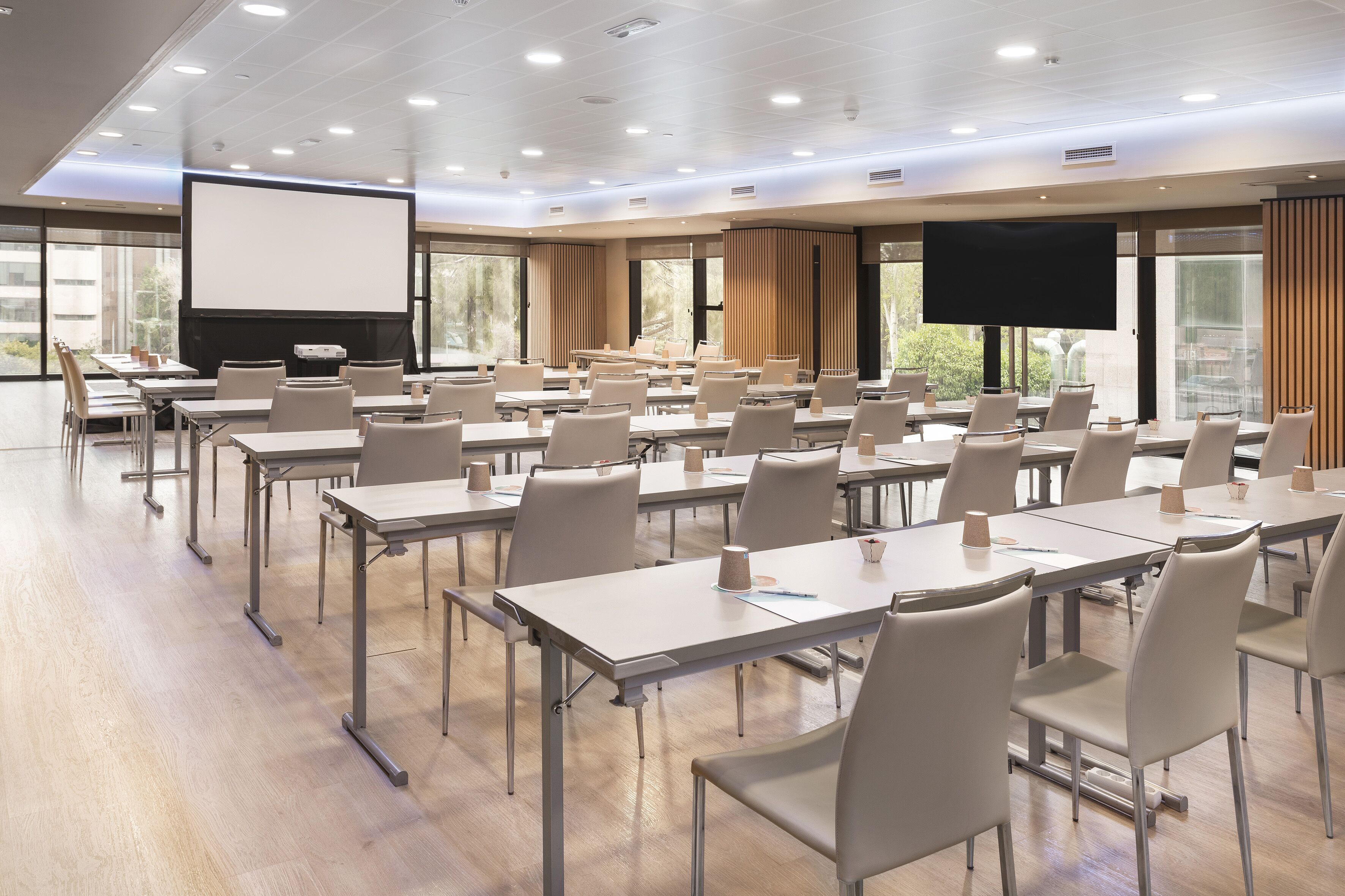 Una sala conferenze con tavoli e sedie, uno schermo grande e finestre con tende.