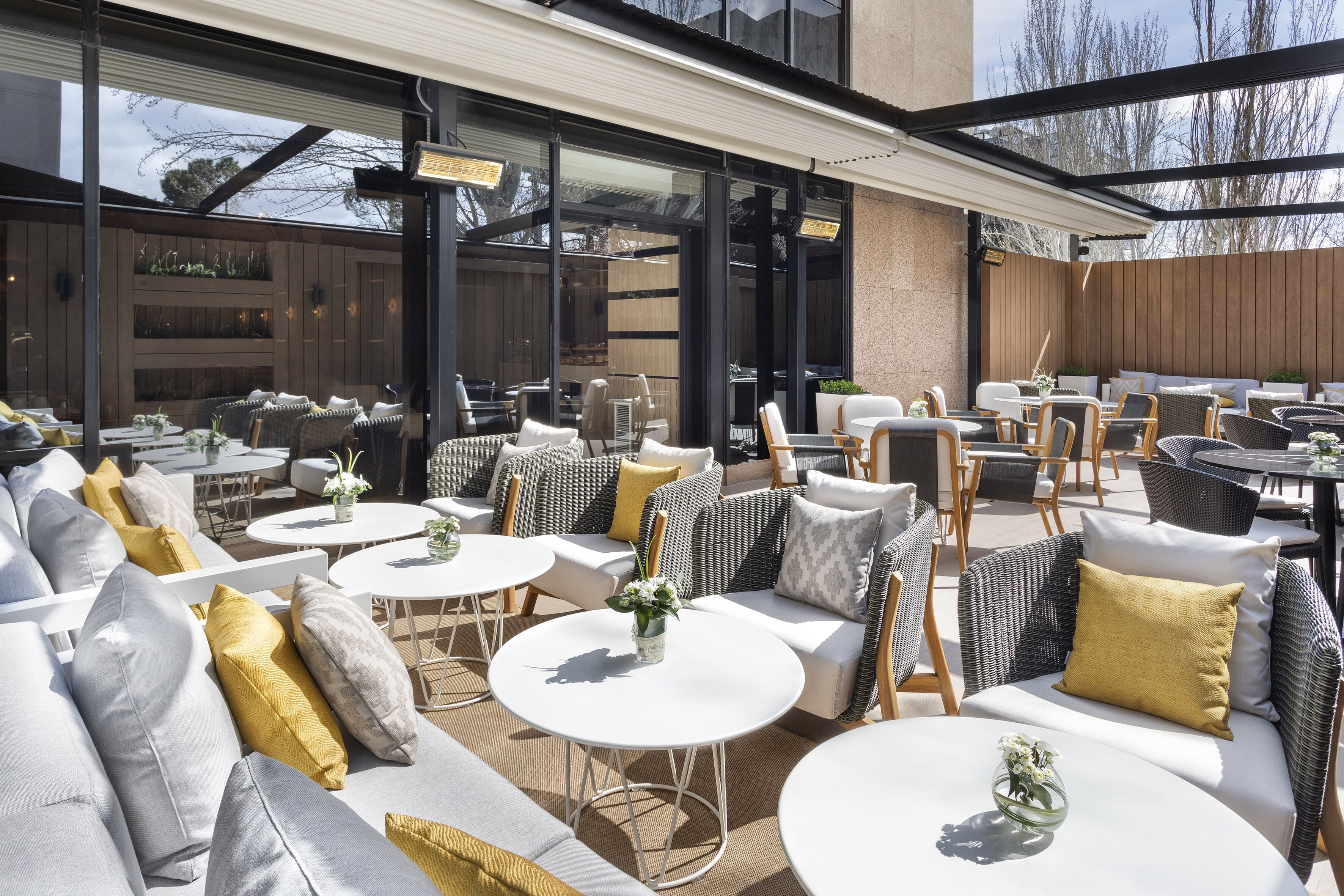 An outdoor patio area with round tables and cushioned seating, large windows, and a covered section.