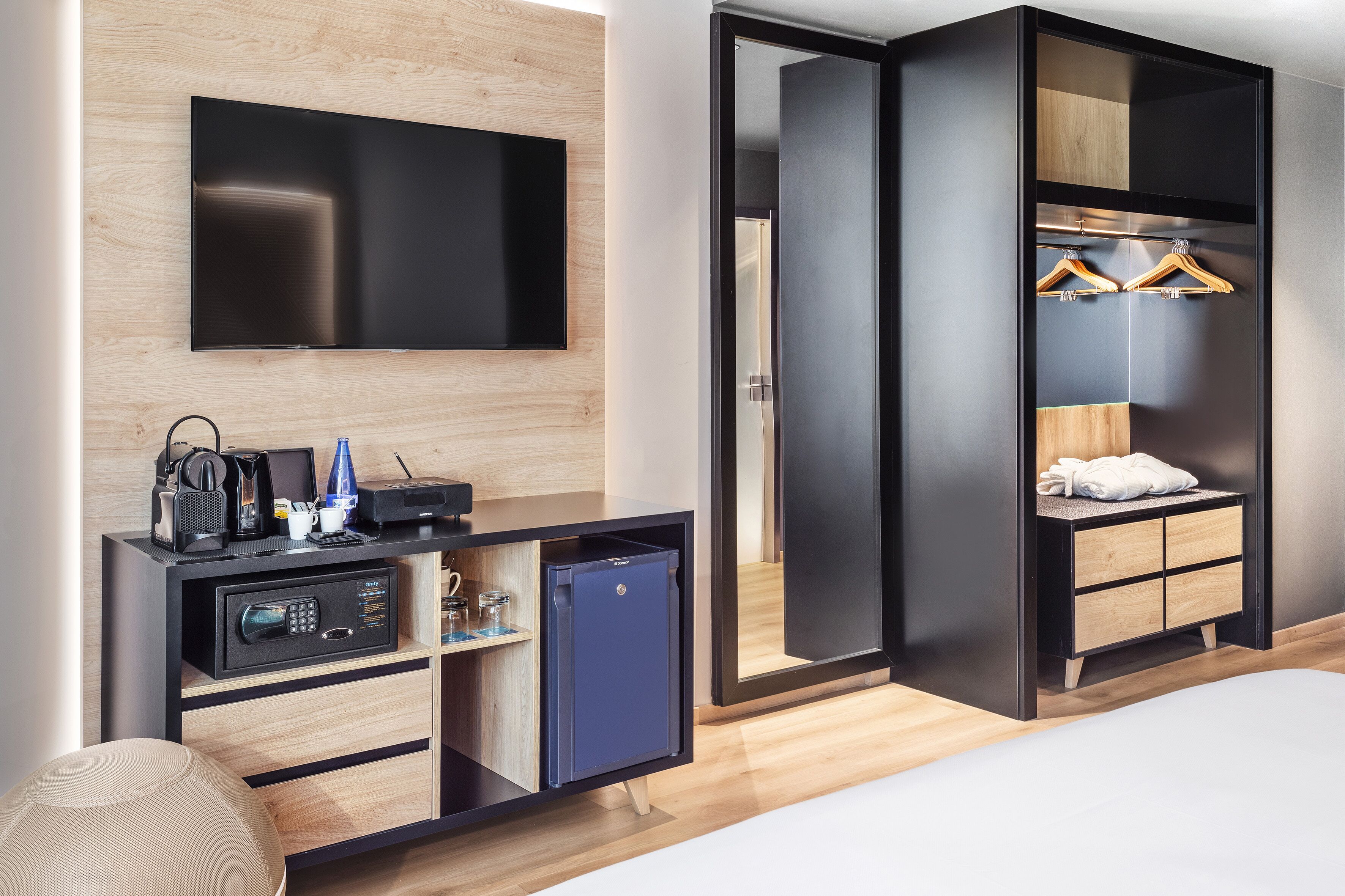 Een moderne hotelkamer met een flatscreen-tv, een minibar, een bureau met koffieapparaat, en een kledingkast met hangruimte.