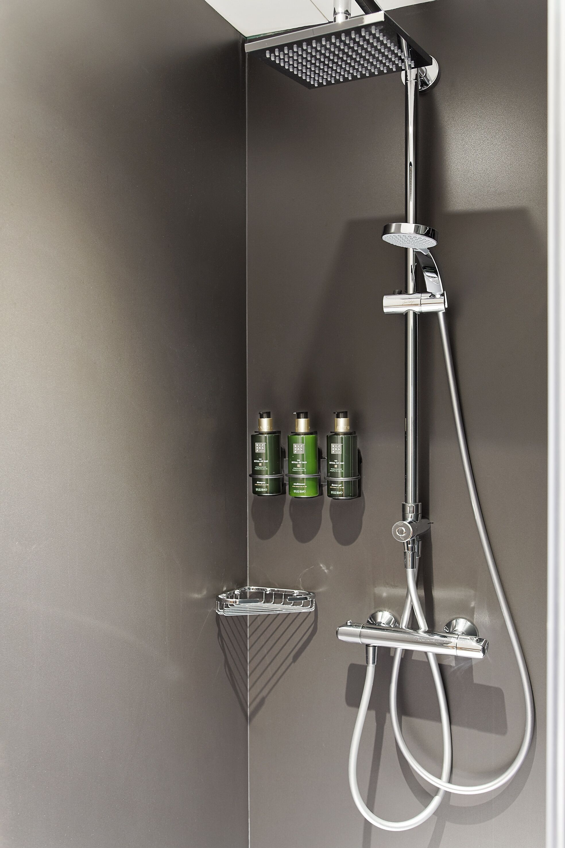Una ducha moderna con cabezal de ducha de mano, cabezal de ducha fijo y un accesorio de ducha de mano. Hay tres botellas de champú y acondicionador en la pared.