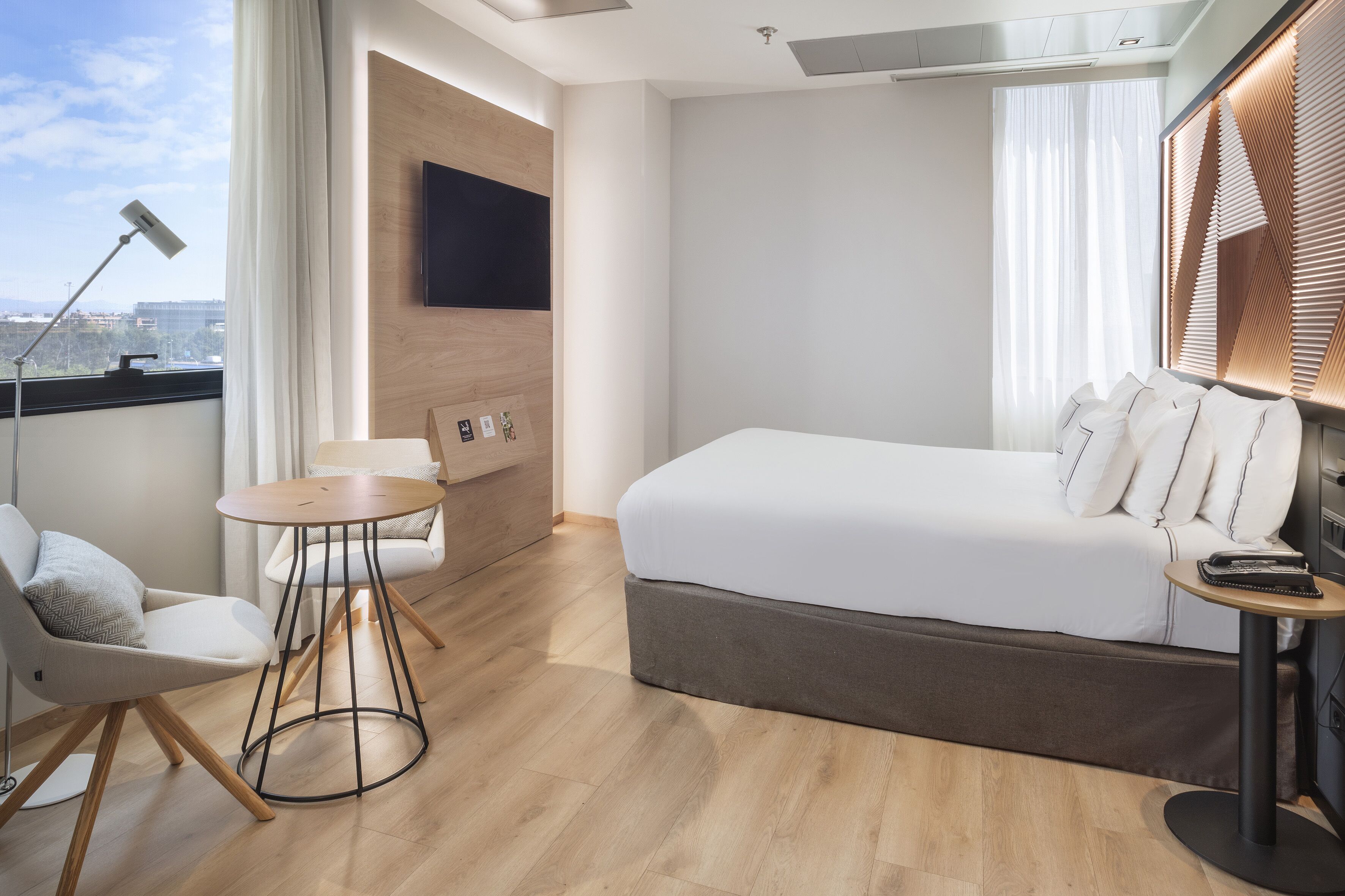 Ein modernes Hotelzimmer mit Bett, Schreibtisch, Stuhl und Wandfernseher.