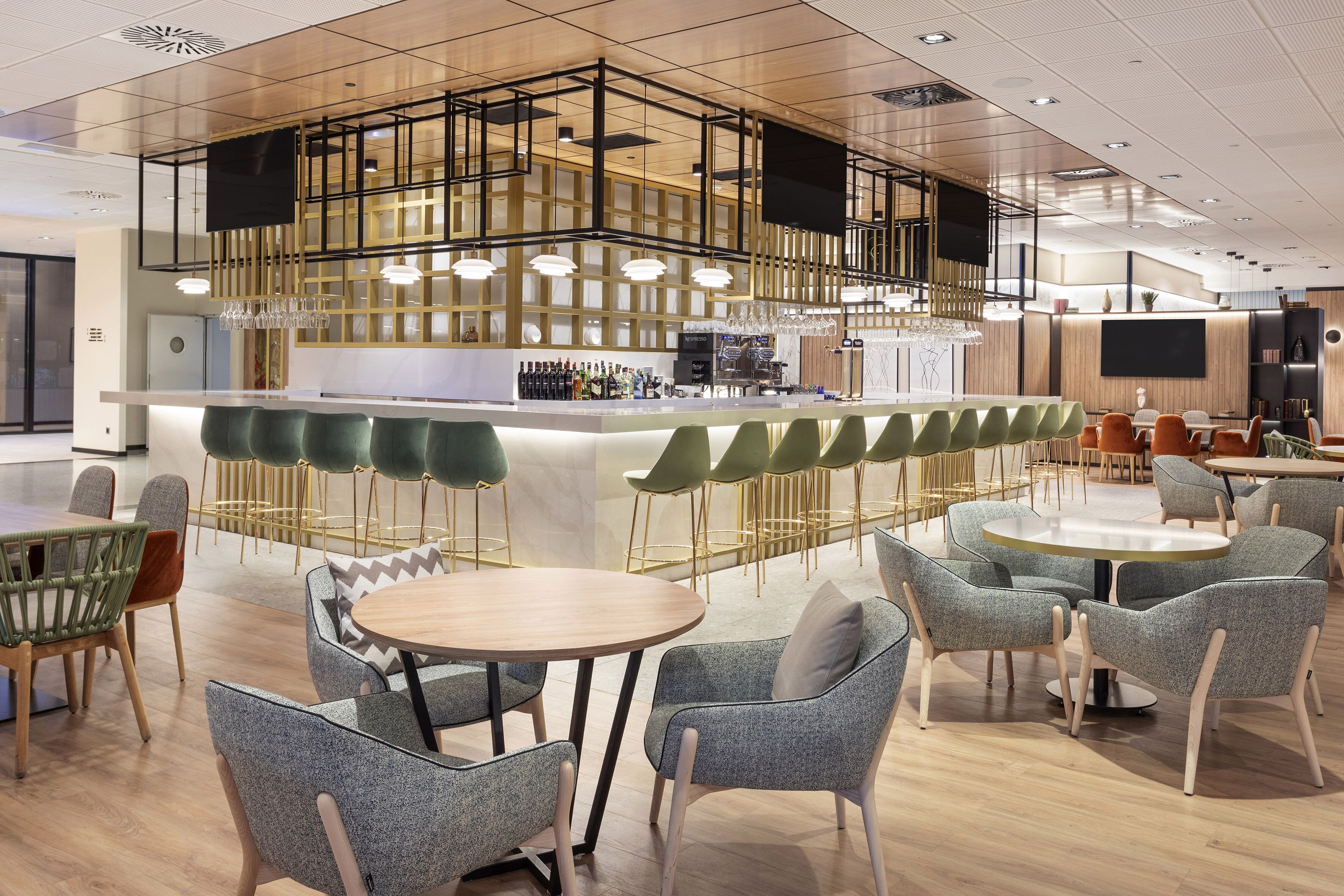 Een moderne bar met een hoge toonbank, barstoelen en diverse zitmogelijkheden, waaronder ronde tafels en stoelen.