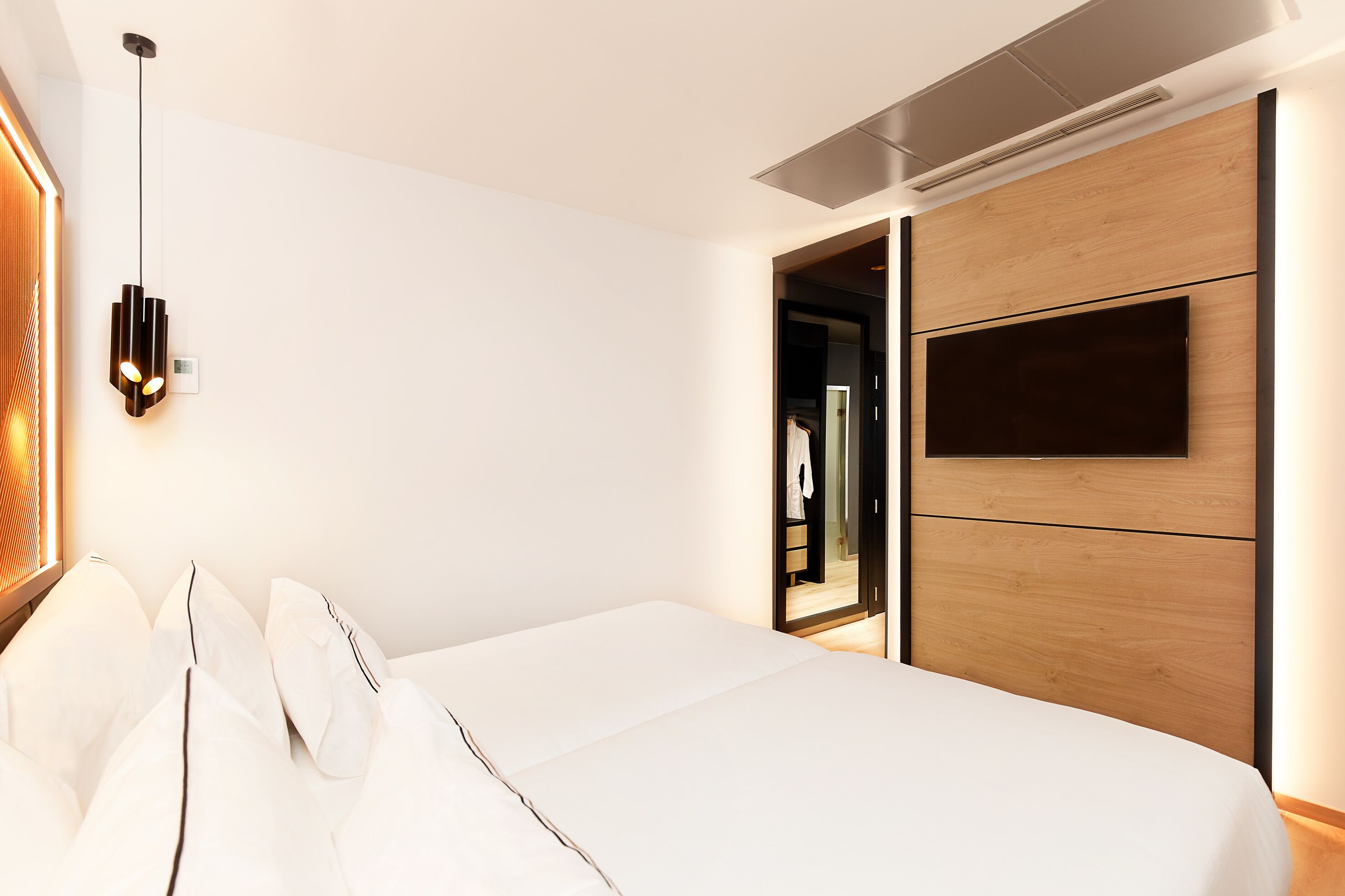 A modern hotel room with a neatly made bed, a wall-mounted TV, and a built-in wardrobe.