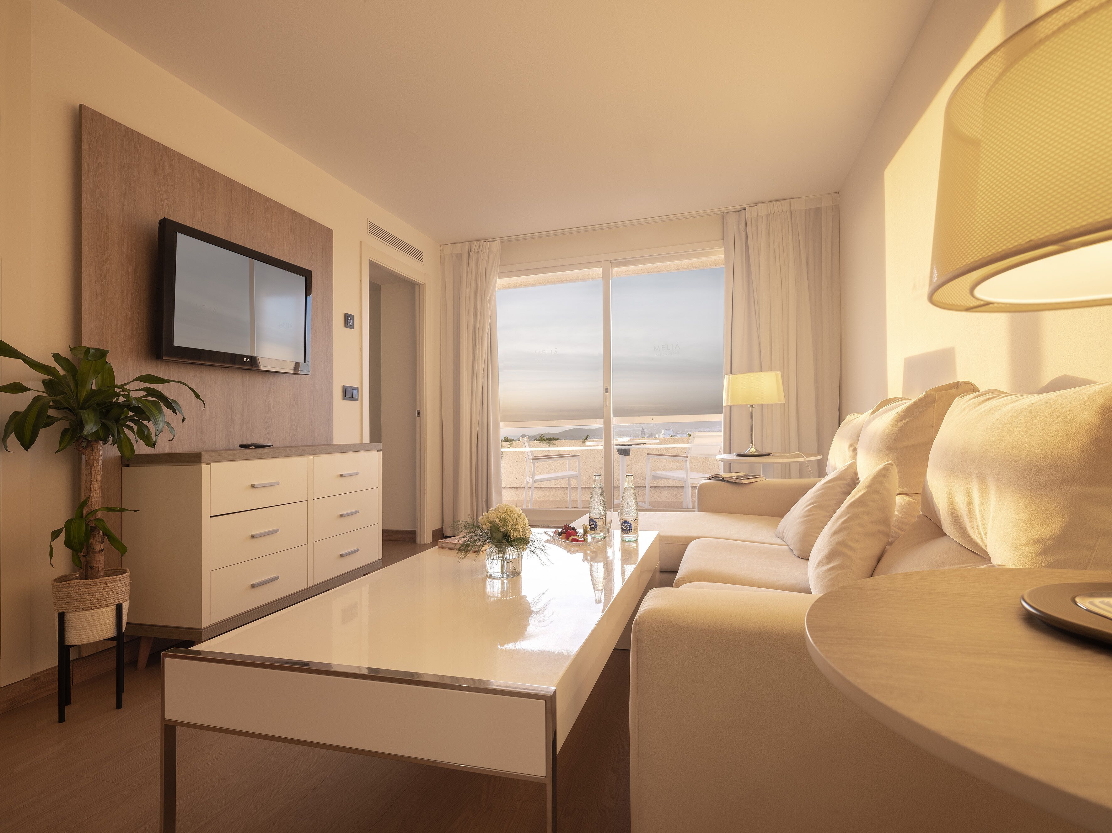 Une chambre d’hôtel moderne dotée d’un téléviseur à écran plat fixé au mur, d’un canapé, d’une table basse et offrant une vue sur la ville grâce à de grandes fenêtres.