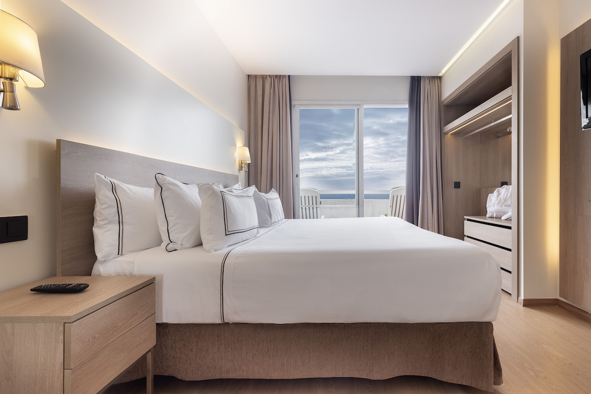 Et moderne hotelværelse med en stor seng, sengeborde, et klædeskab og havudsigt.