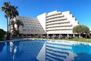 Un hotel con una piscina grande, palmeras y un diseño arquitectónico moderno.