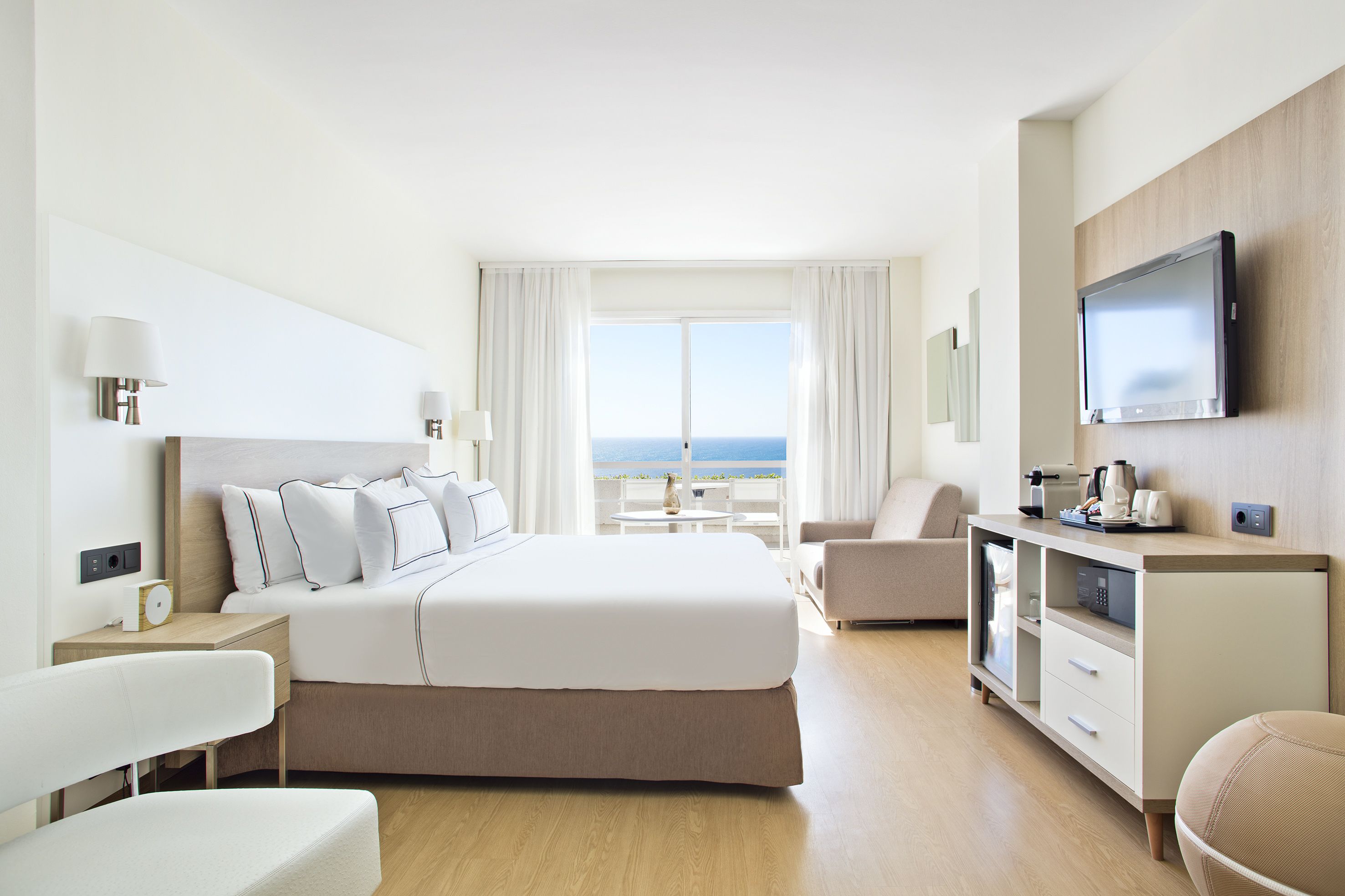 A modern hotel room with a large bed, a desk, a chair, and a television.