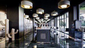 A modern hotel lobby with a reflective marble floor, a cactus sculpture, and a coffee machine. - Melia Sitges (Sitges)
