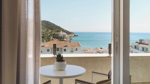 A balcony with a table and chairs, overlooking a coastal town with buildings and a clear view of the sea. - Melia Sitges (Sitges)