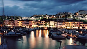 A marina with boats docked, buildings with balconies, and a calm water surface reflecting the lights. - Melia Sitges (Sitges)