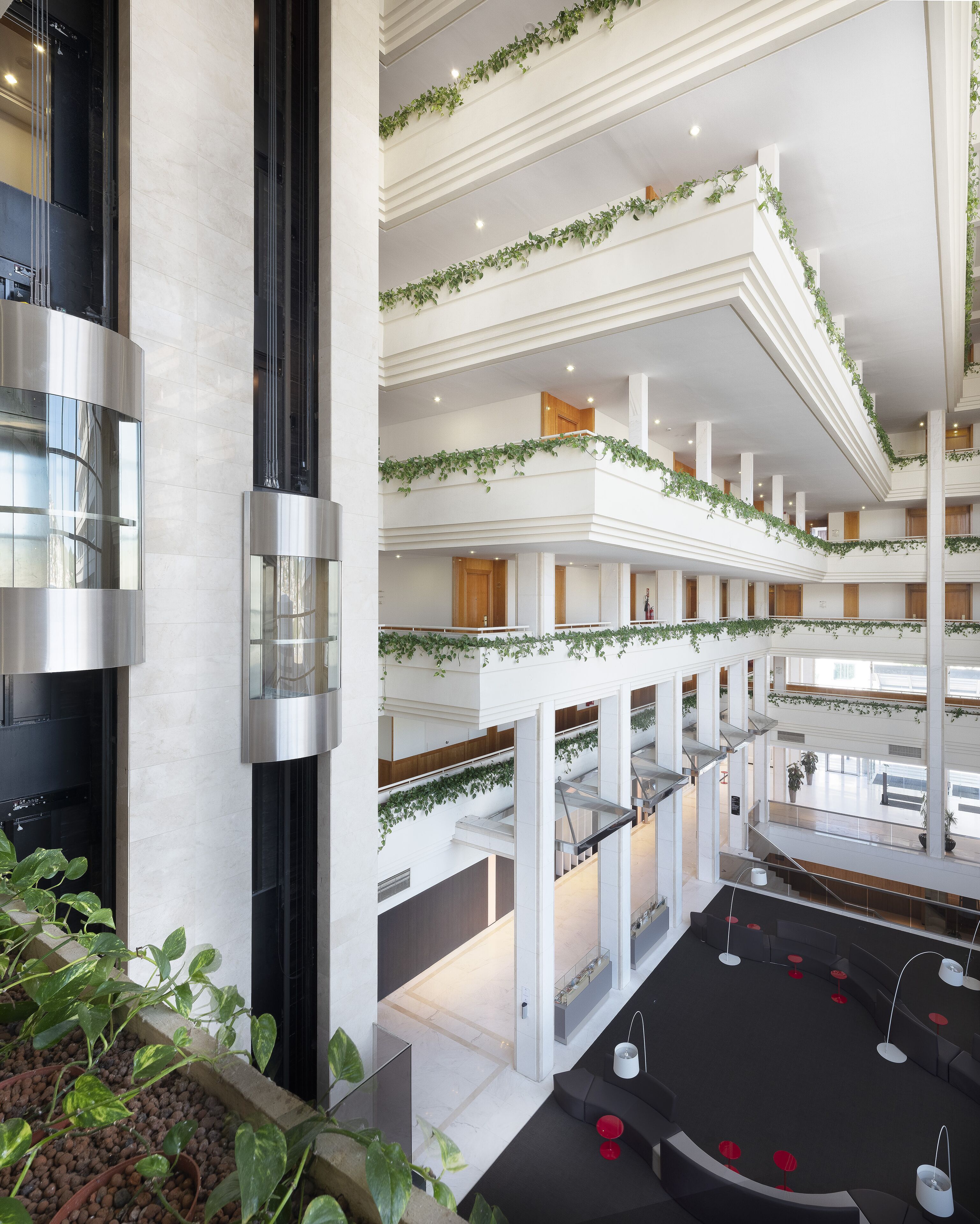 A multi-level atrium with a central staircase, white walls, and green plants.