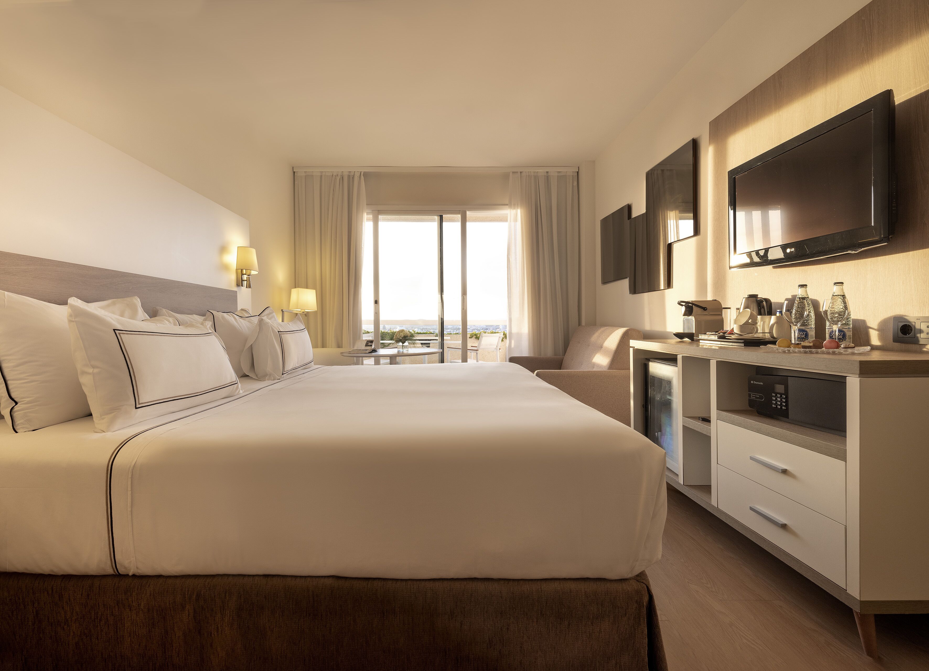Ein Hotelzimmer mit einem großen Bett, einem Schreibtisch mit Flachbildfernseher und Blick ins Freie.