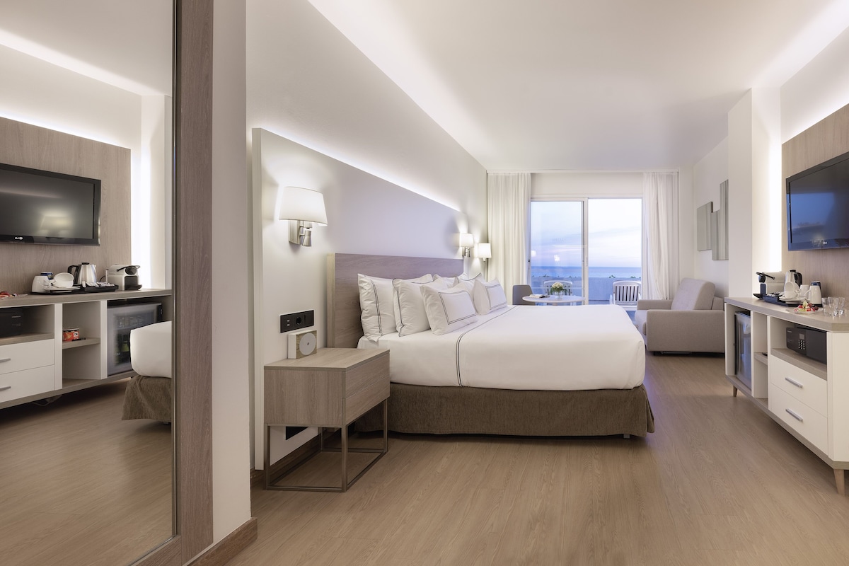 Et moderne hotelværelse med en stor seng, et skrivebord, et fjernsyn og havudsigt.