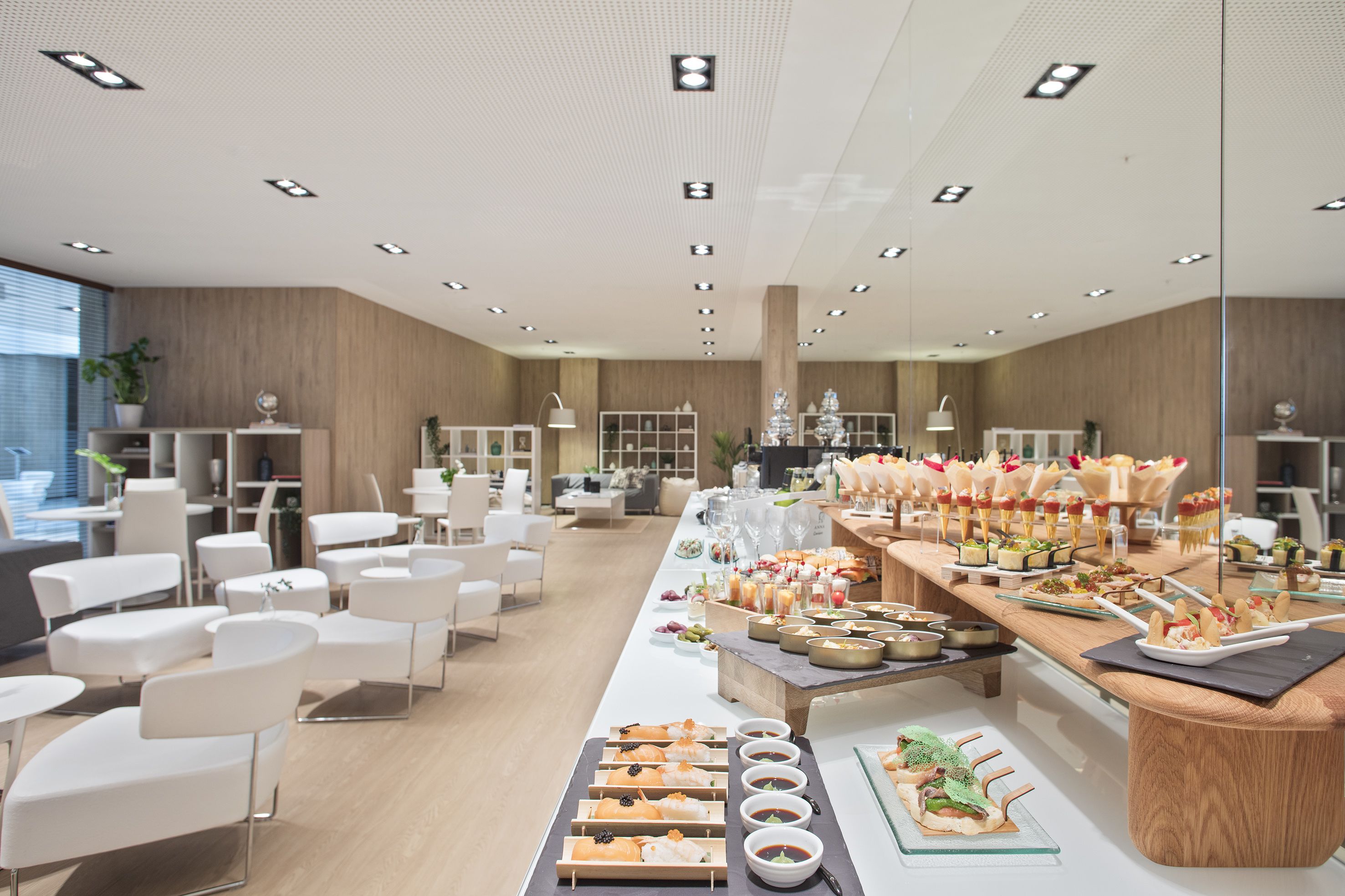 Een moderne hotellobby met een lange buffettafel, witte stoelen en een houten receptiebalie.