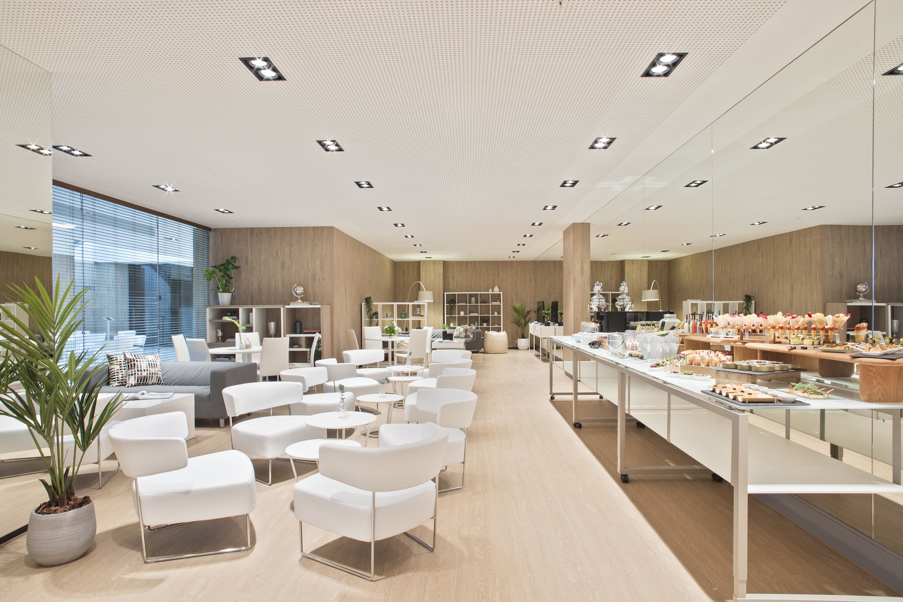 Eine moderne Hotelhalle mit weißen Möbeln, einer langen Rezeption und einem Essbereich mit Speisenauslage.