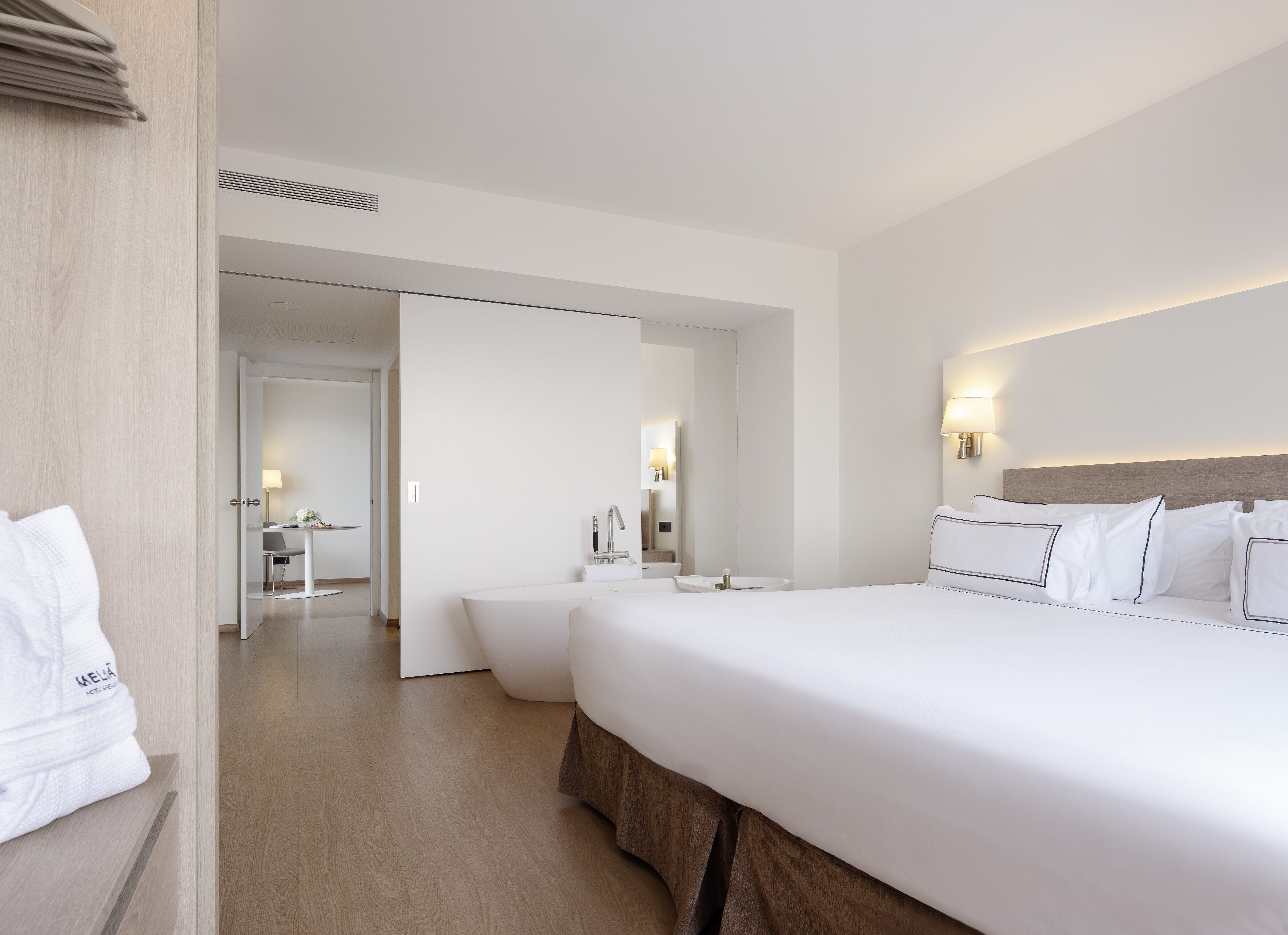 Una habitación de hotel moderna con una cama grande, una mesita de noche, un espejo y un baño visible a través de una puerta abierta.
