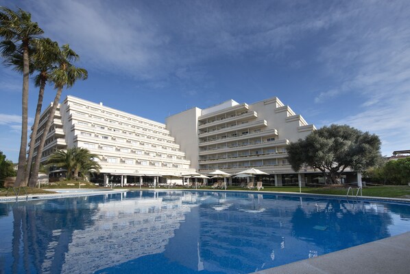 Un hotel con piscina, varias plantas y sombrillas exteriores.