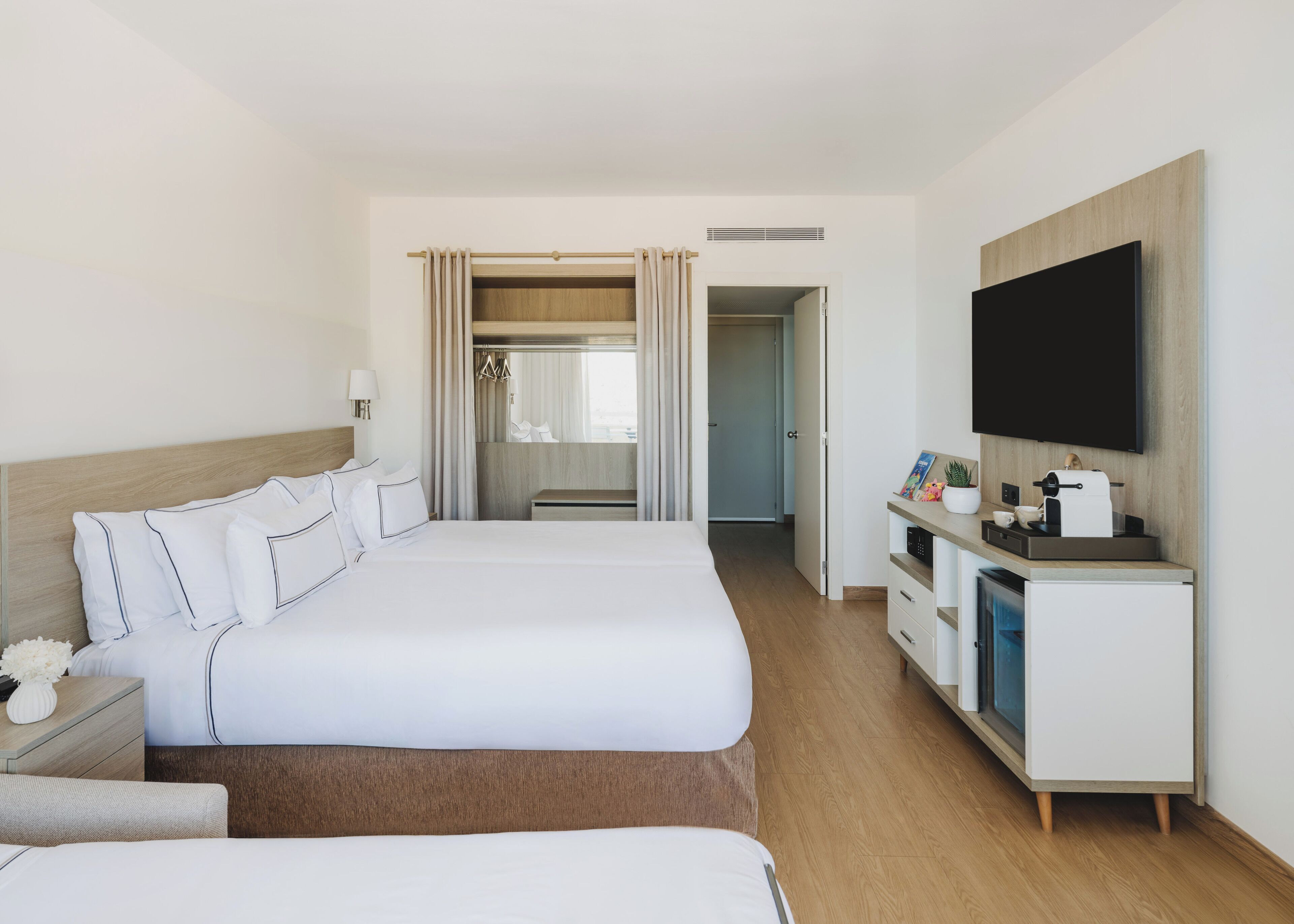 Une chambre d’hôtel avec un grand lit, une télévision, un bureau avec une machine à café et un dressing.