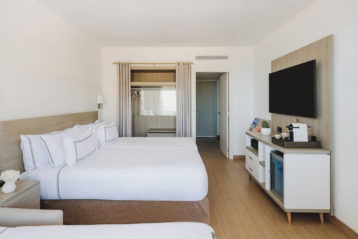 Et hotelværelse med en stor seng, et fjernsyn, et skrivebord med kaffemaskine og et walk-in closet.