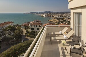 Un balcón con mesa y sillas, con vistas a un pueblo costero con edificios y una vista despejada del mar.