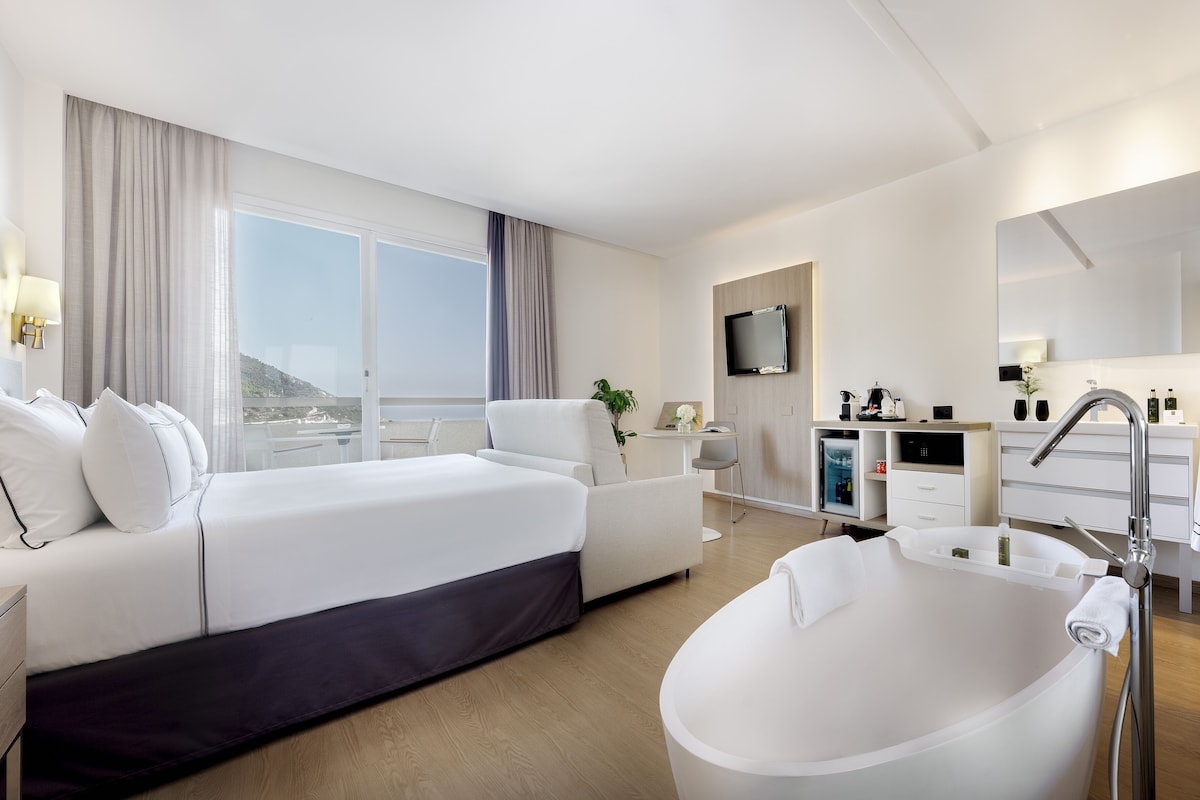 Et moderne hotelværelse med en stor seng, et separat siddeområde, et badekar, et fjernsyn og udsigt ud