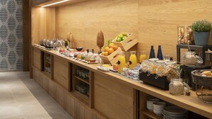 Un bufé de desayuno con diversos alimentos y bebidas, paneles de madera en las paredes y piso de baldosas.