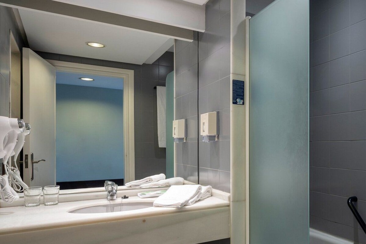 Une salle de bain moderne avec un grand miroir, un lavabo doté d’un porte-serviettes et un espace douche.