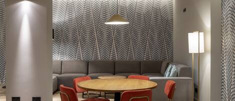 A modern dining area with a round wooden table, red upholstered chairs, and a grey sofa.