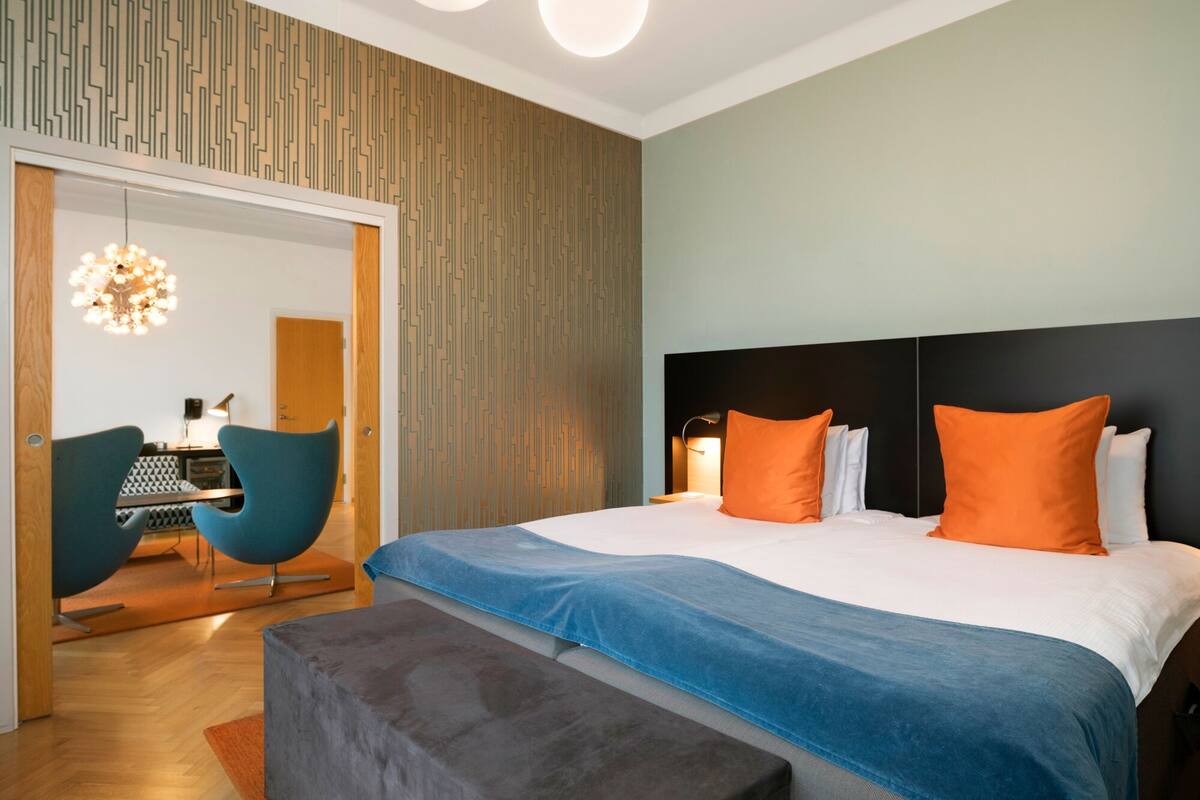 A modern hotel room with a large bed, a desk with a chair, and a unique patterned wall.