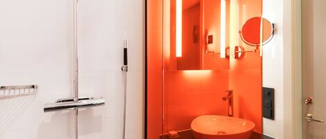 A modern bathroom with a glass-enclosed shower, a round mirror, and a sink with a red basin.