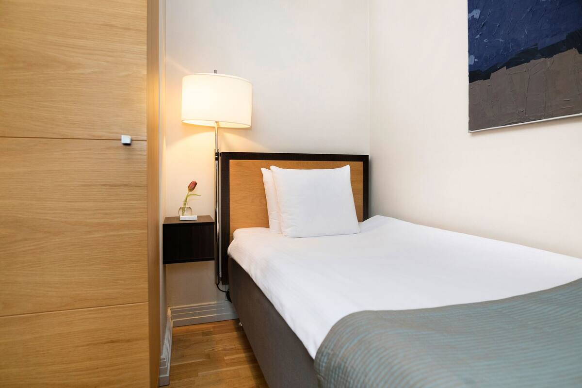 A hotel room with a bed, a nightstand, a lamp, and a painting on the wall.